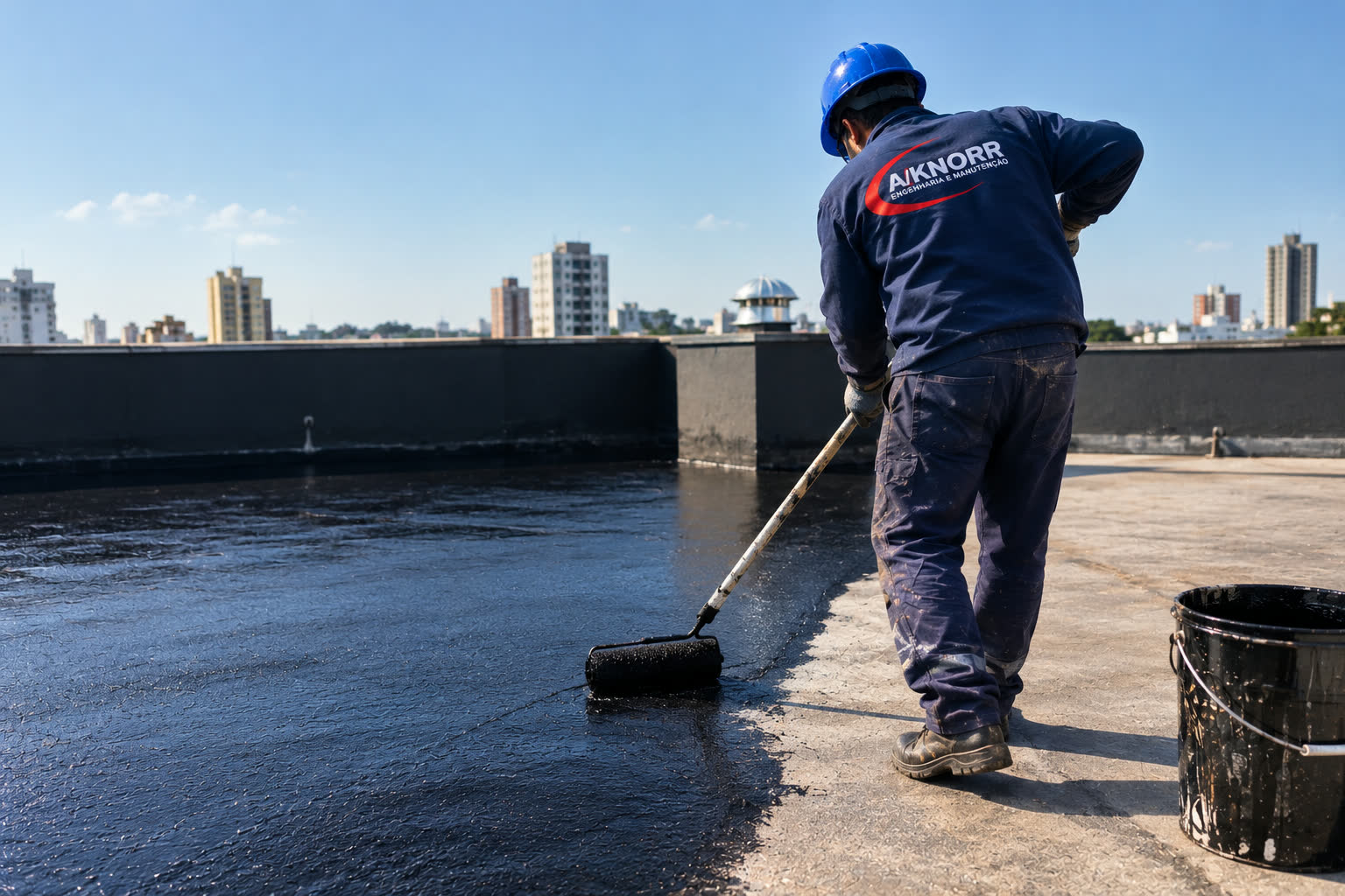 Técnico da A/KNORR aplicando impermeabilizante líquido com rolo de extensão sobre laje plana de cobertura, com o skyline da cidade ao fundo