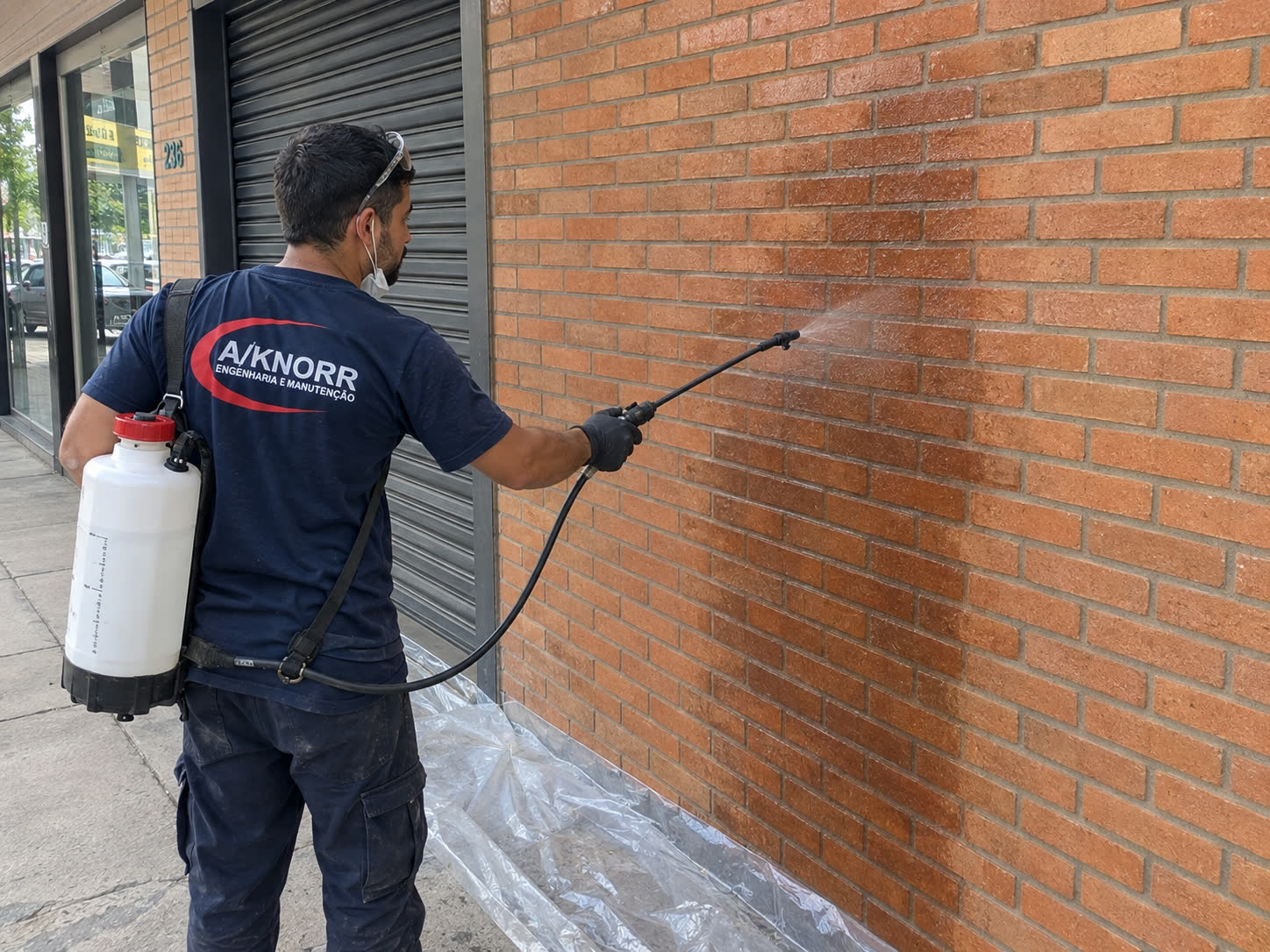 Técnico da A/KNORR aplicando hidrorrepelente com pulverizador em parede de tijolo aparente